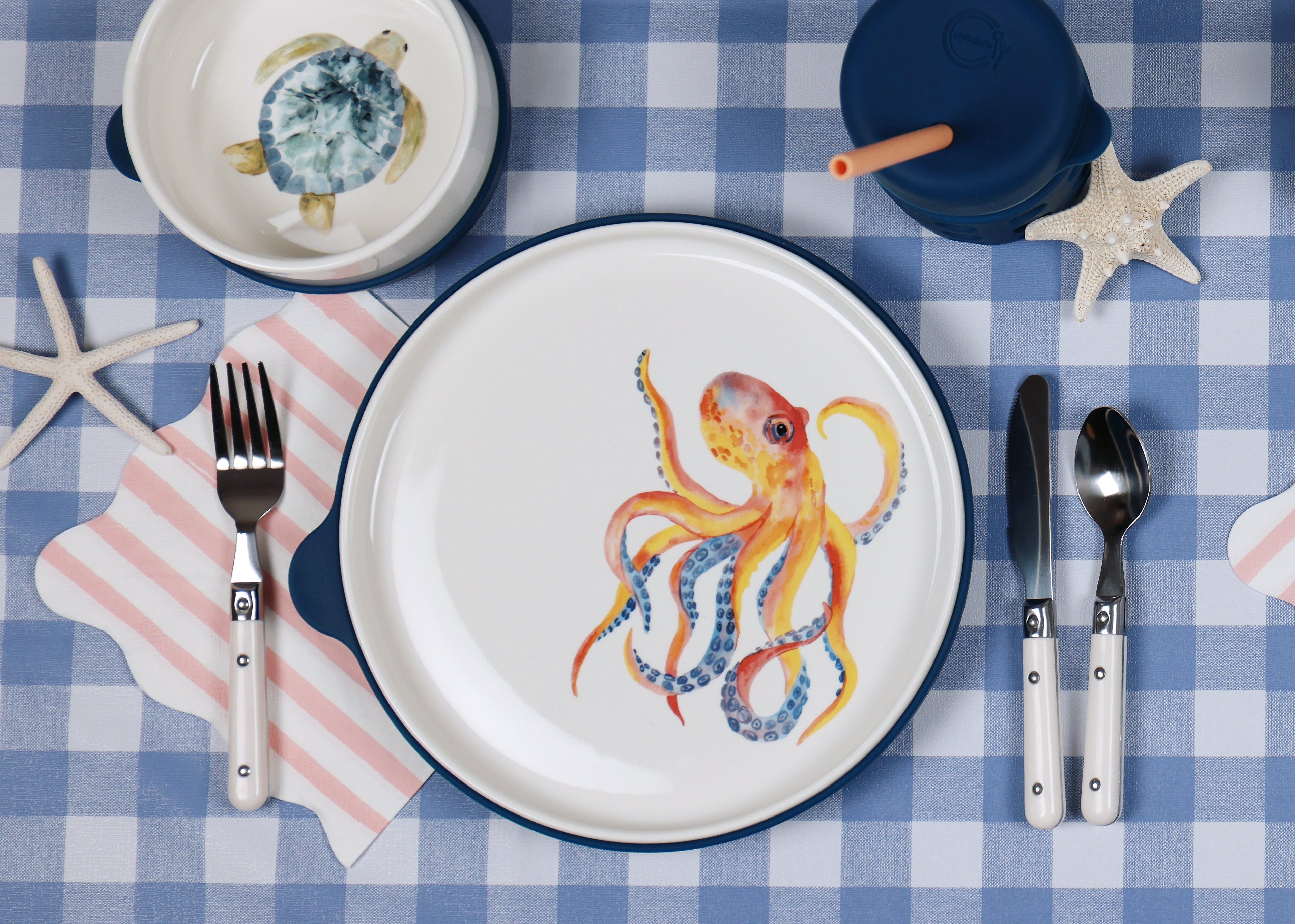 Table setting with ceramic plates featuring marine designs on a blue checkered tablecloth.