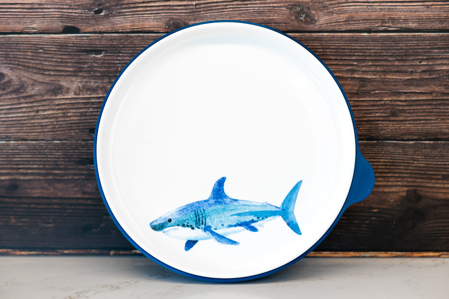 Kids' ceramic dinner plate with a watercolor shark illustration and a silicone base for stability and durability.