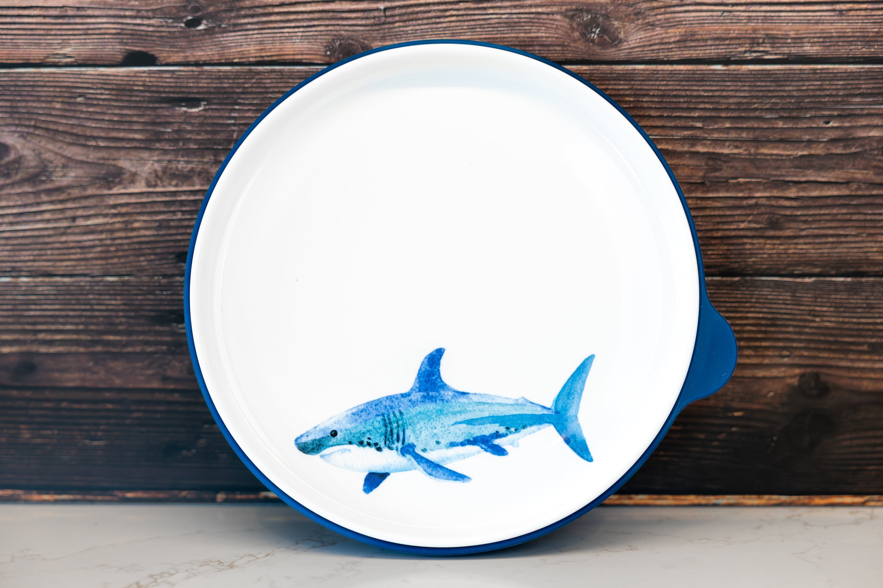 Kids' ceramic dinner plate with a watercolor shark illustration and a silicone base for stability and durability.