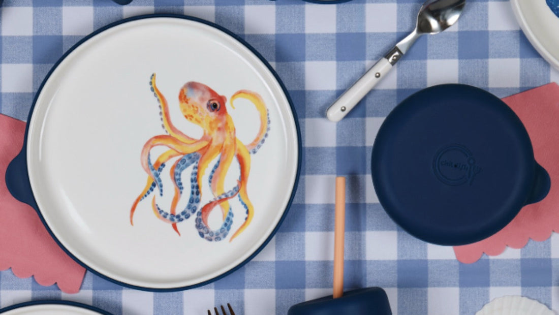 Table setting with ceramic plates, cups, and cutlery on a blue checkered tablecloth.